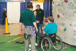 Mark Wellman helps LaWanda Cook, BRS, prepare to climb the wall as staff from the Adventure Wall observes